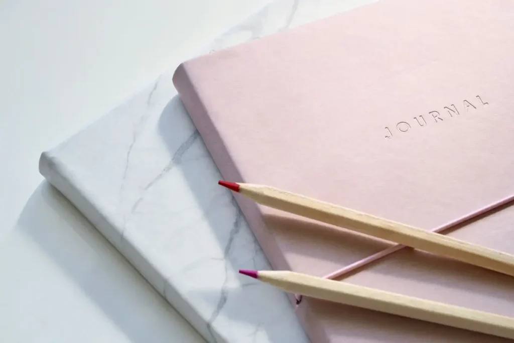 white and pink journal with two colored pencils